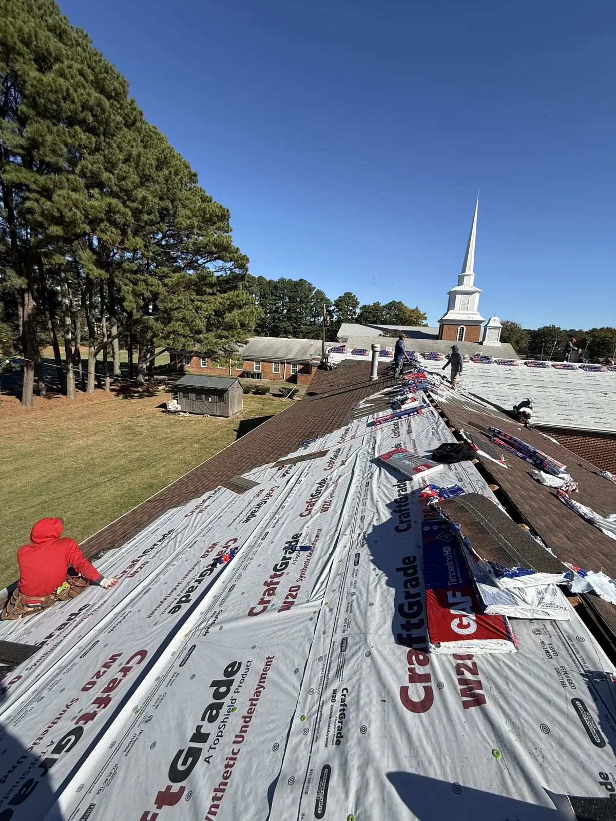 Underlayment and shingle bundles across a church roof, steeple in the background
