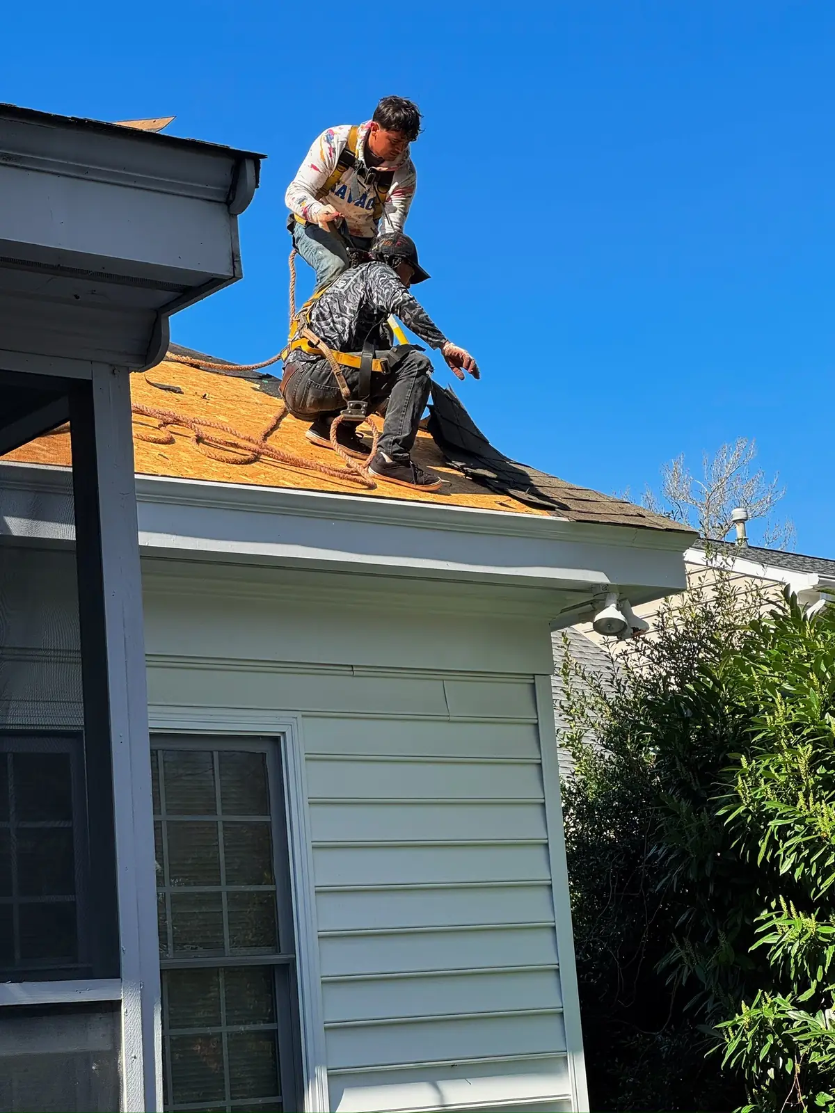 Two RoofTrue roofers working on bare decking at the eave of a two-story home