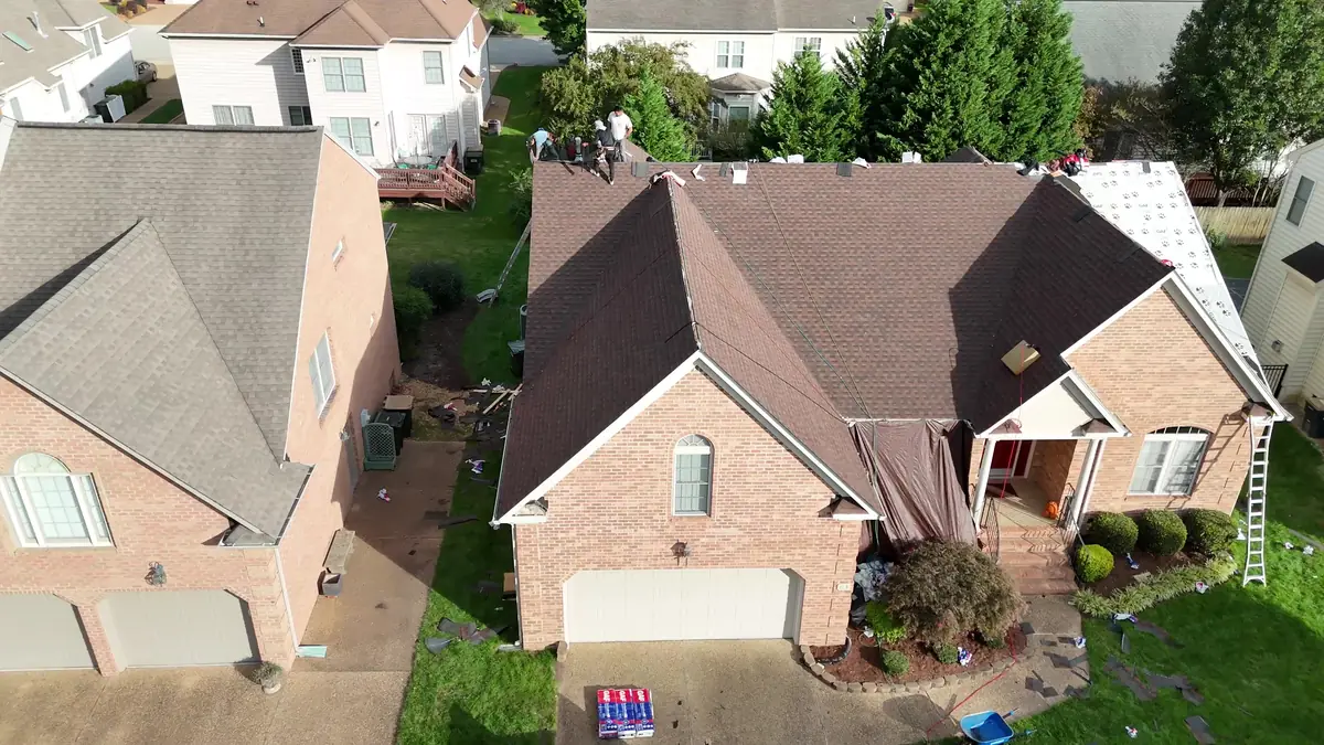 Overhead drone view of a brick home with a brown shingle roof and ladders set at the eaves