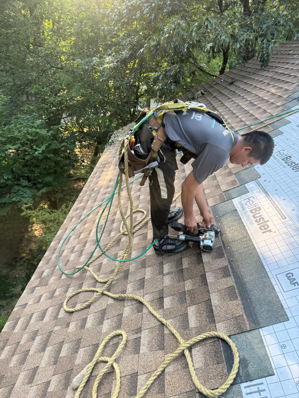 Roofer in a harness installing shingles over GAF FeltBuster underlayment