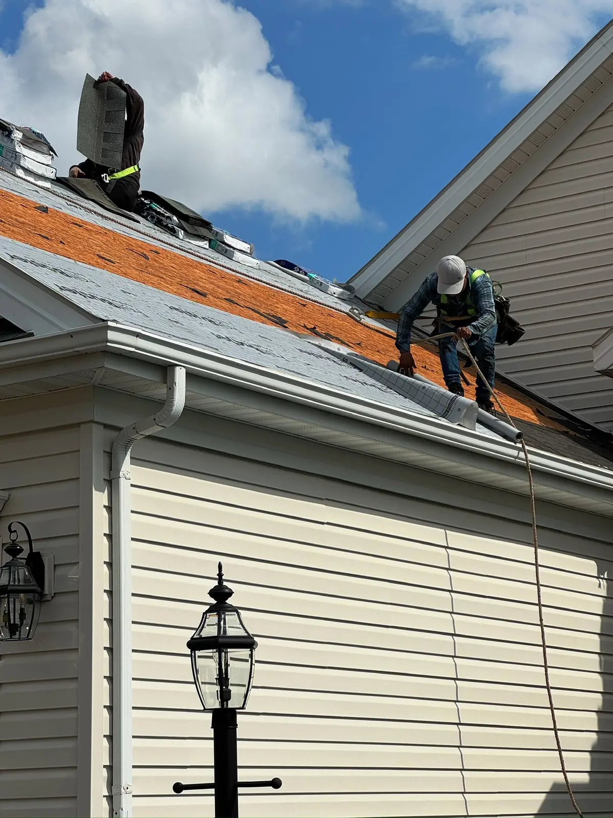 Roofers working on a partly torn-off roof above tan siding
