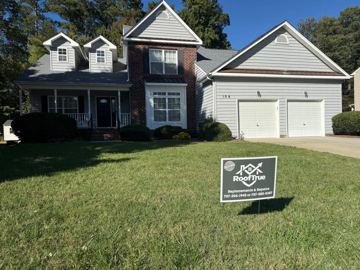 Two-story brick and gray-siding home with a new gray shingle roof and a RoofTrue yard sign on the lawn