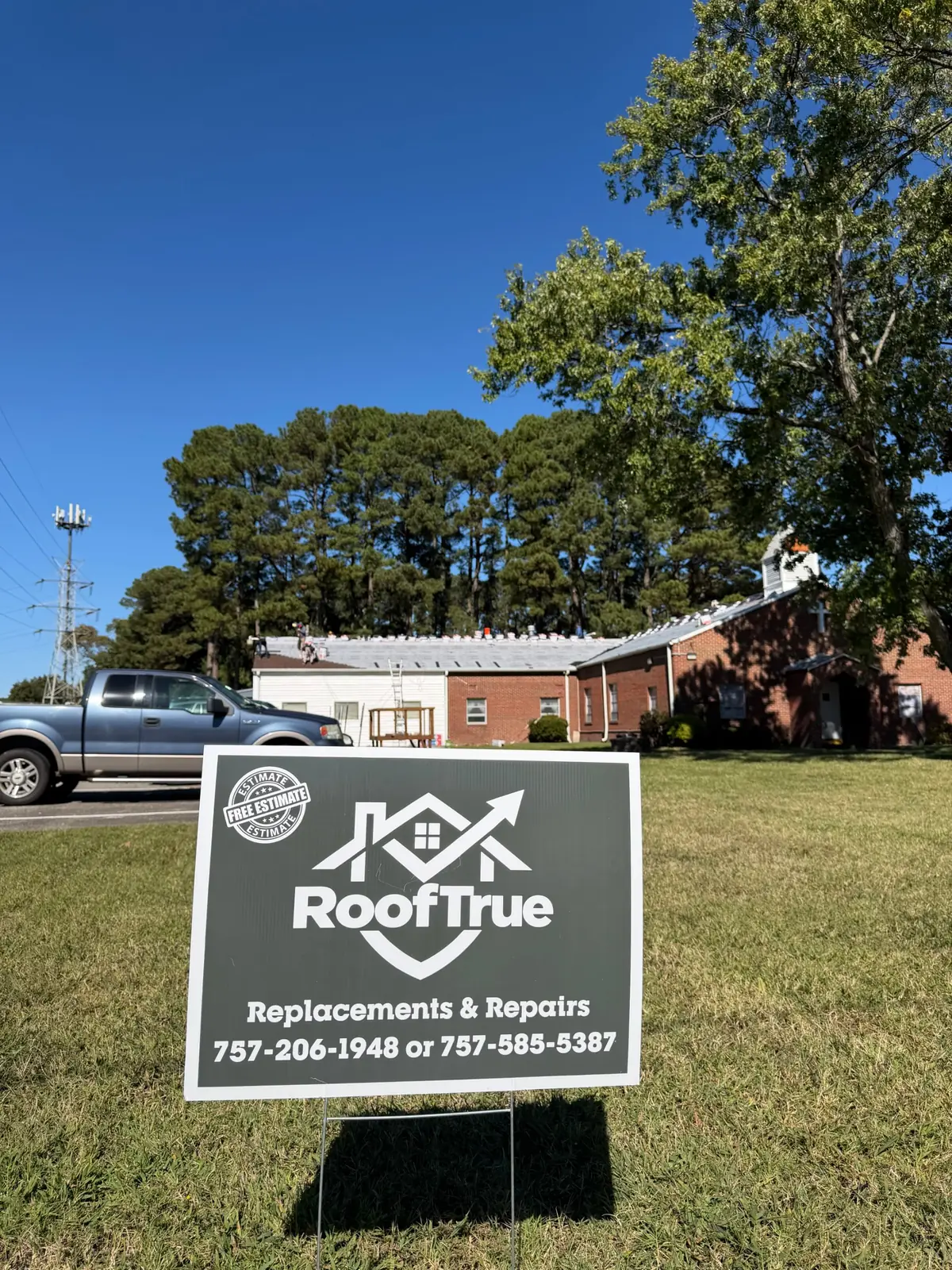 RoofTrue yard sign on the lawn of a brick church while the crew works on the roof