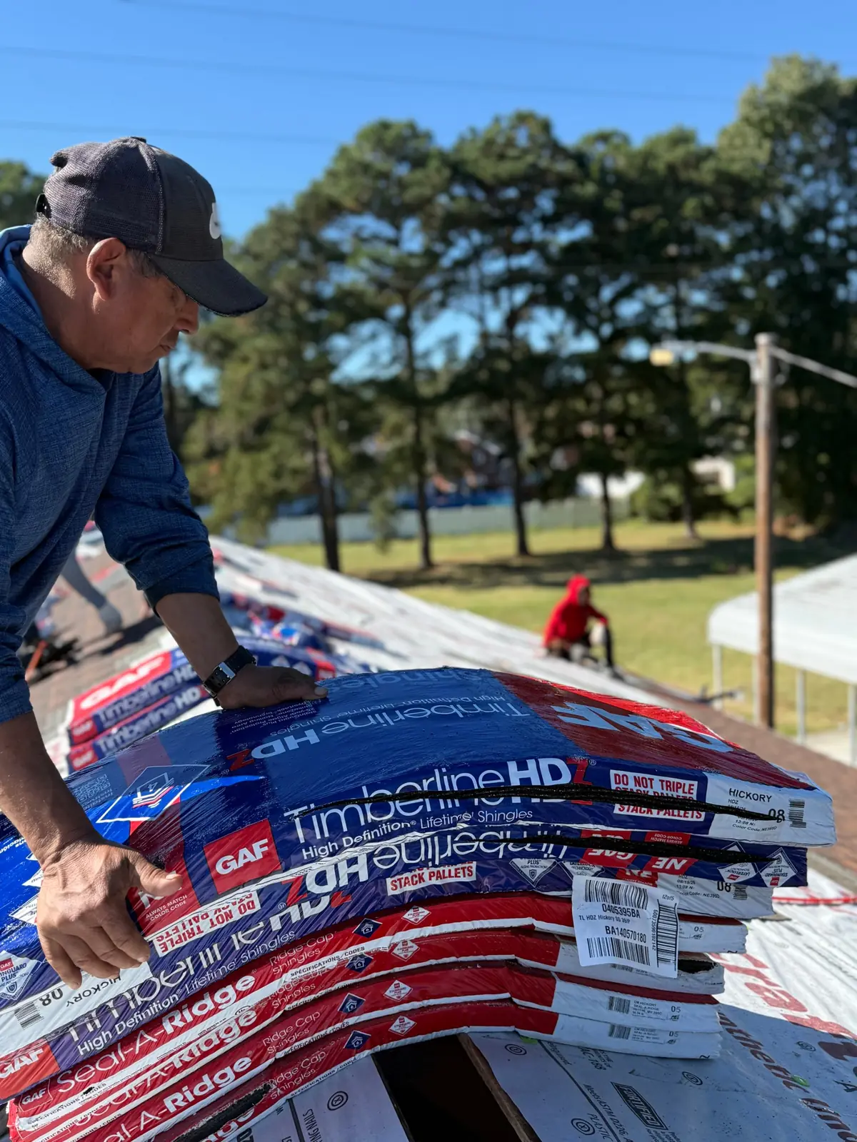Roofer stacking GAF Timberline HDZ shingles in Hickory and Seal-A-Ridge cap shingles on a roof